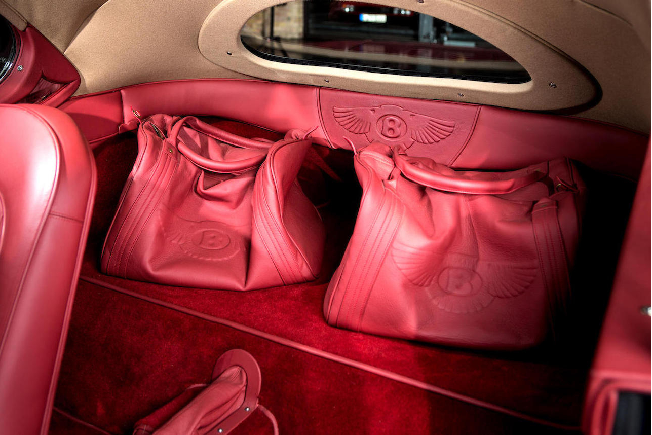 Interior is in tasteful red leather and comes with matching bags.
